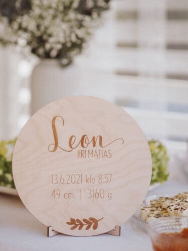 Birch plywood birth board on which the child's birth information is engraved with a party table in the background.