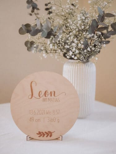 Birch plywood birth board engraved with the child's birth information, with a flower arrangement in the background.
