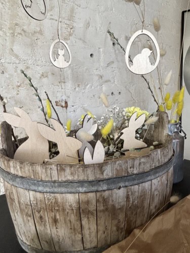 Kuvassa pääsiäisasetelma, jossa on puinen kori täynnä vaneripupuja ja yläpuolella kolme pääsiäismunaa