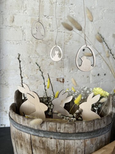 Kuvassa pääsiäisasetelma, jossa on puinen kori täynnä vaneripupuja ja yläpuolella kolme pääsiäismunaa